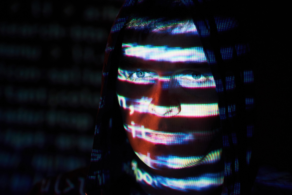 צילום תקריב של תוקף סייבר עם פנים מוסתרות בגלל השתקפות אור של מסך מחשב