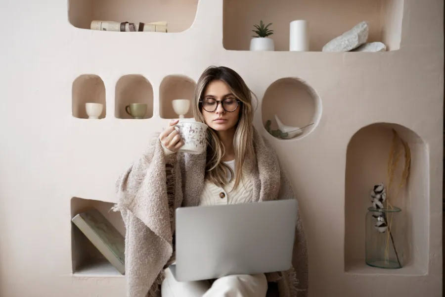 אישה עצמאית עם משקפיים יושבת עם מחשב נייד ועובדת ועושה הכנסה