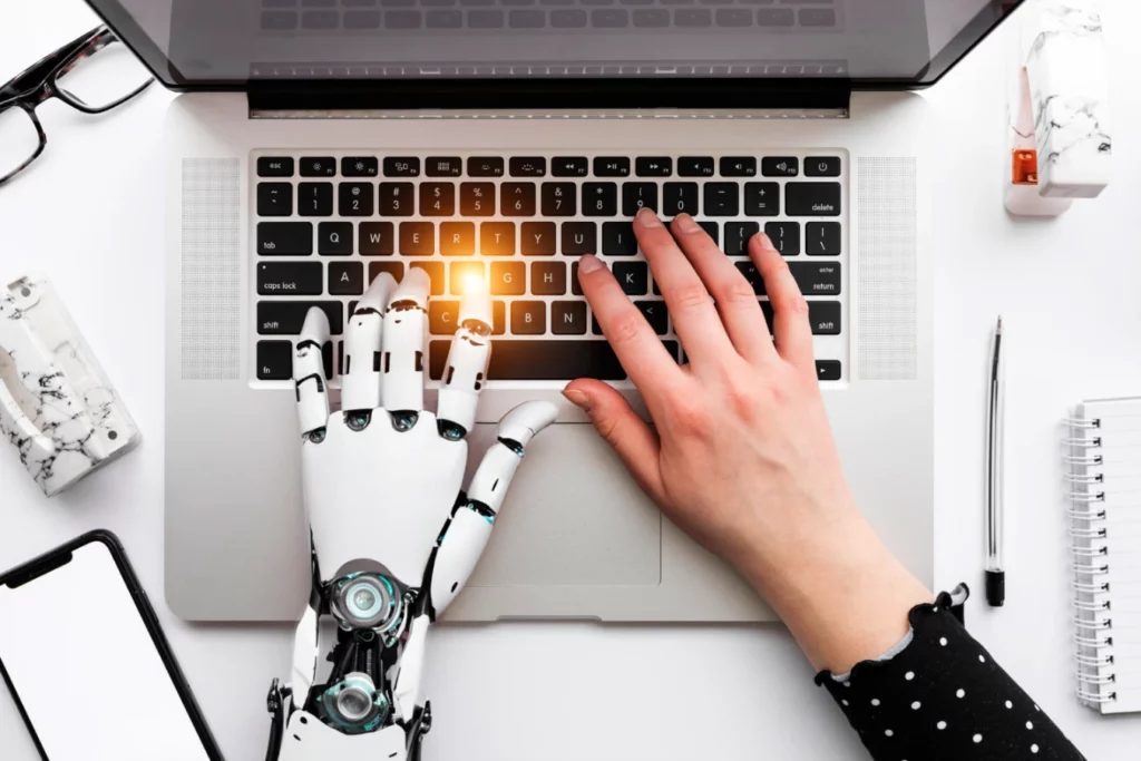 יד אנושית ויד רובוטית מניחות ידיים על מחשב נייד כשיתוף פעולה מנצח